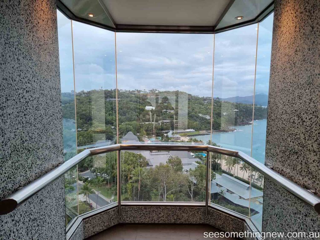 View from the Hamilton Island Reef View Hotel Lift of palm tree fringed beach with an azure sea behind it and mountan islands in the background.