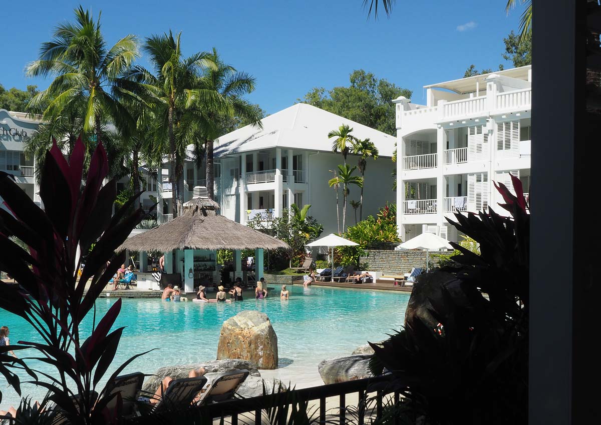 View across lagoon pool to swim up pool bar with thatched roof and people ordering at the bar at peppers palm cove